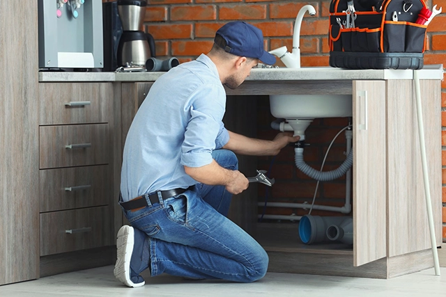 Plumber Fixing Sink in Modern Kitchen Cabinet, Focus on Plumbing Service